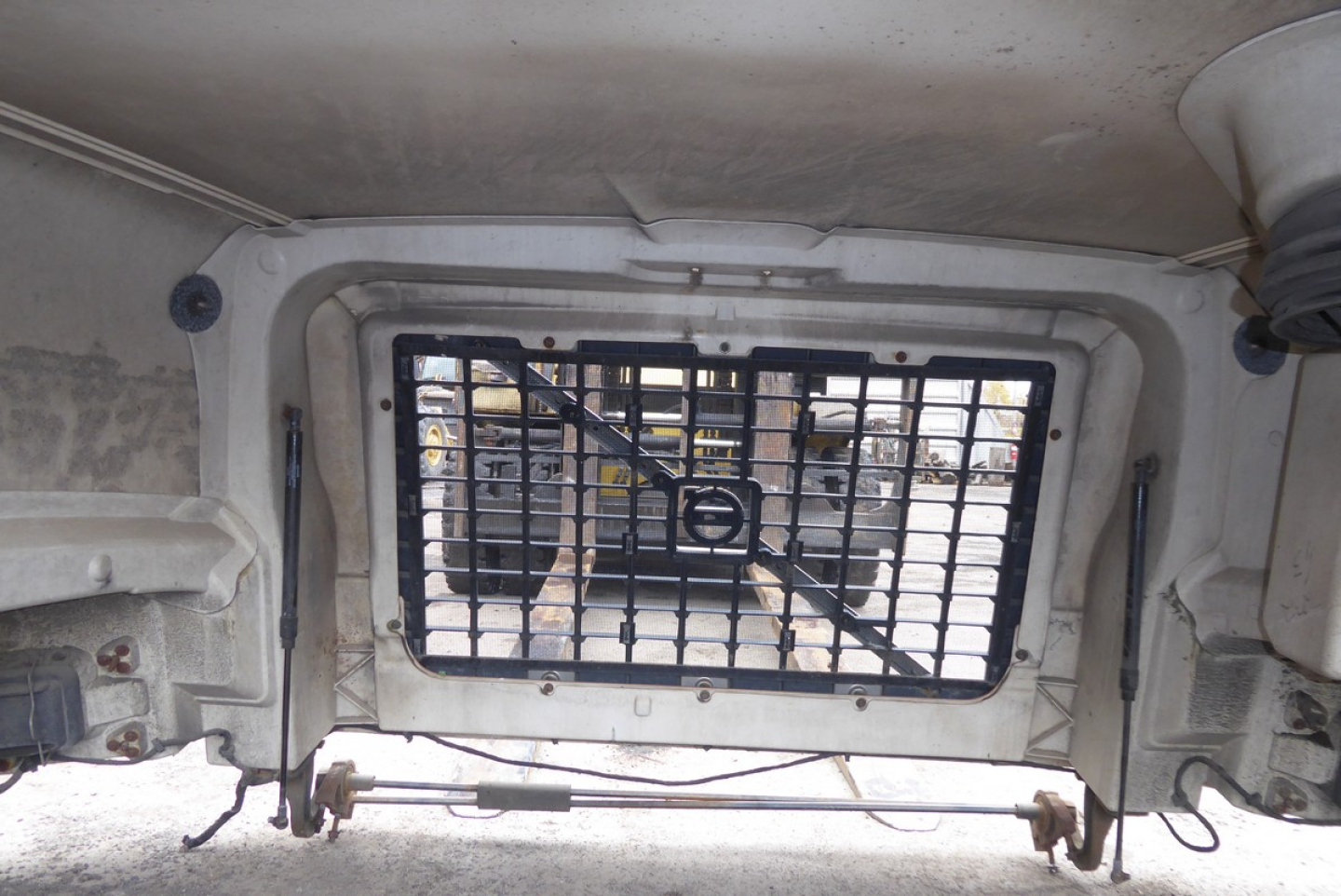 Truck hood area showing a ventilated window with a metal grille inside the hood of a Volvo VNM.