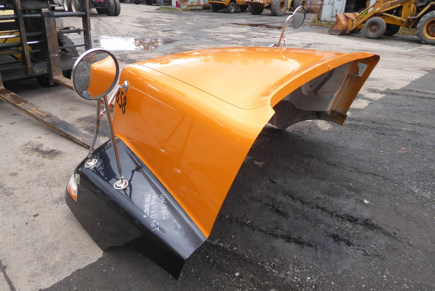 Orange Volvo VNM hood piece with mounting hardware, truck parts in yard.
