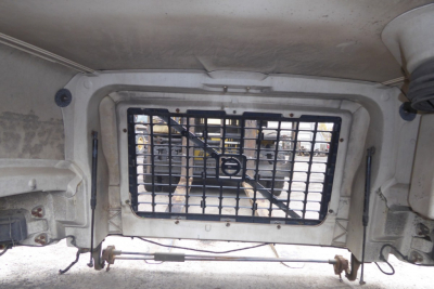 Truck hood area showing a ventilated window with a metal grille inside the hood of a Volvo VNM.