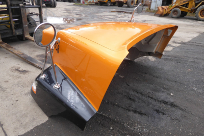 Orange Volvo VNM hood piece with mounting hardware, truck parts in yard.