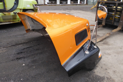 Orange Volvo hood/cover assembly for a Volvo VNM shows vent grille and windshield wiper area. Part of a truck hood with hinge area visible.