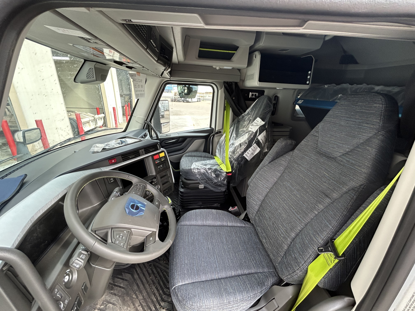 Volvo VNL64T860 cab interior showing steering wheel, dashboard, captain seats, overhead storage, and seating with seat belts.