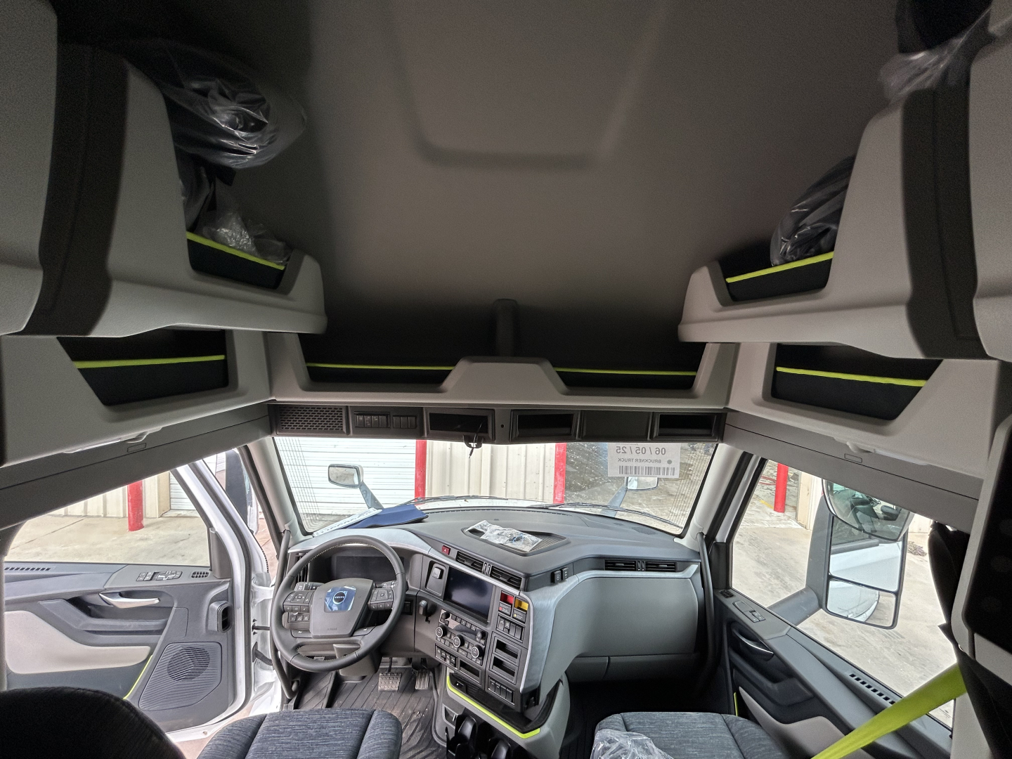 Truck cab interior from driver's seat showing dashboard, steering wheel, and overhead sleeper storage with cargo nets.