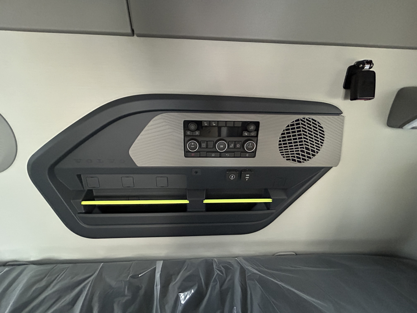 Truck interior ceiling panel with control console, two air vents with yellow accents, circular speaker grille, and buttons.