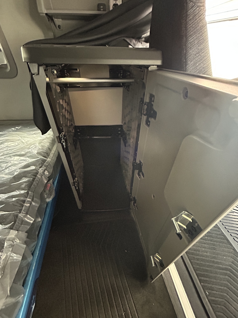 Volvo VNL64T860 sleeper cab interior showing open cabinet with storage compartments and hinges, view from cab floor to side panel.