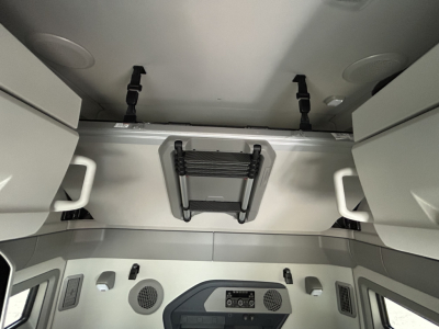 Volvo VNL64T860 sleeper cab interior showing overhead storage with latches and a foldable ladder/step in center, light gray panels, and ceiling mounts.