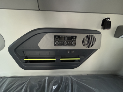 Truck interior ceiling panel with control console, two air vents with yellow accents, circular speaker grille, and buttons.