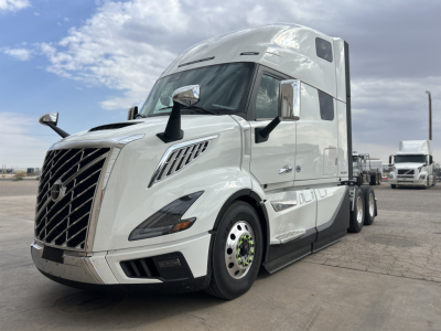 Truck cab with Volvo emblem, front grille, and side mirrors; white 2026 Volvo VNL64T860 with aerodynamic features and chrome accents.