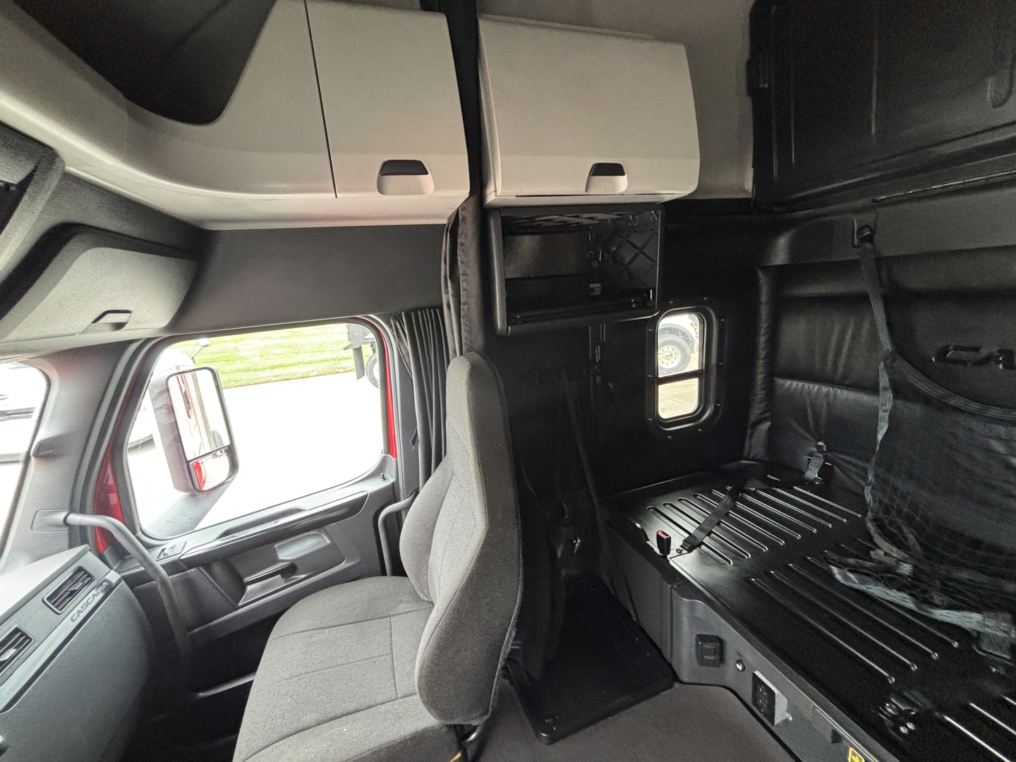 Cab interior with sleeper area and storage compartments in a Freightliner truck showing dashboard and seating.