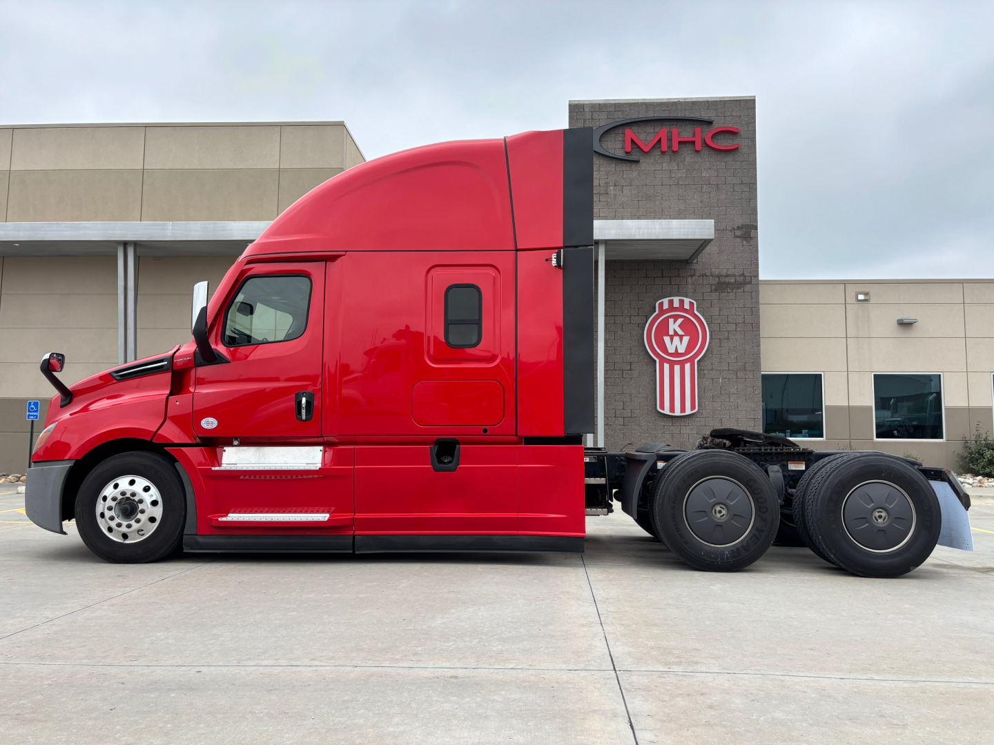 Freightliner PT126064ST truck side view showing red cab and black fifth wheel area with KW truck logo in background.