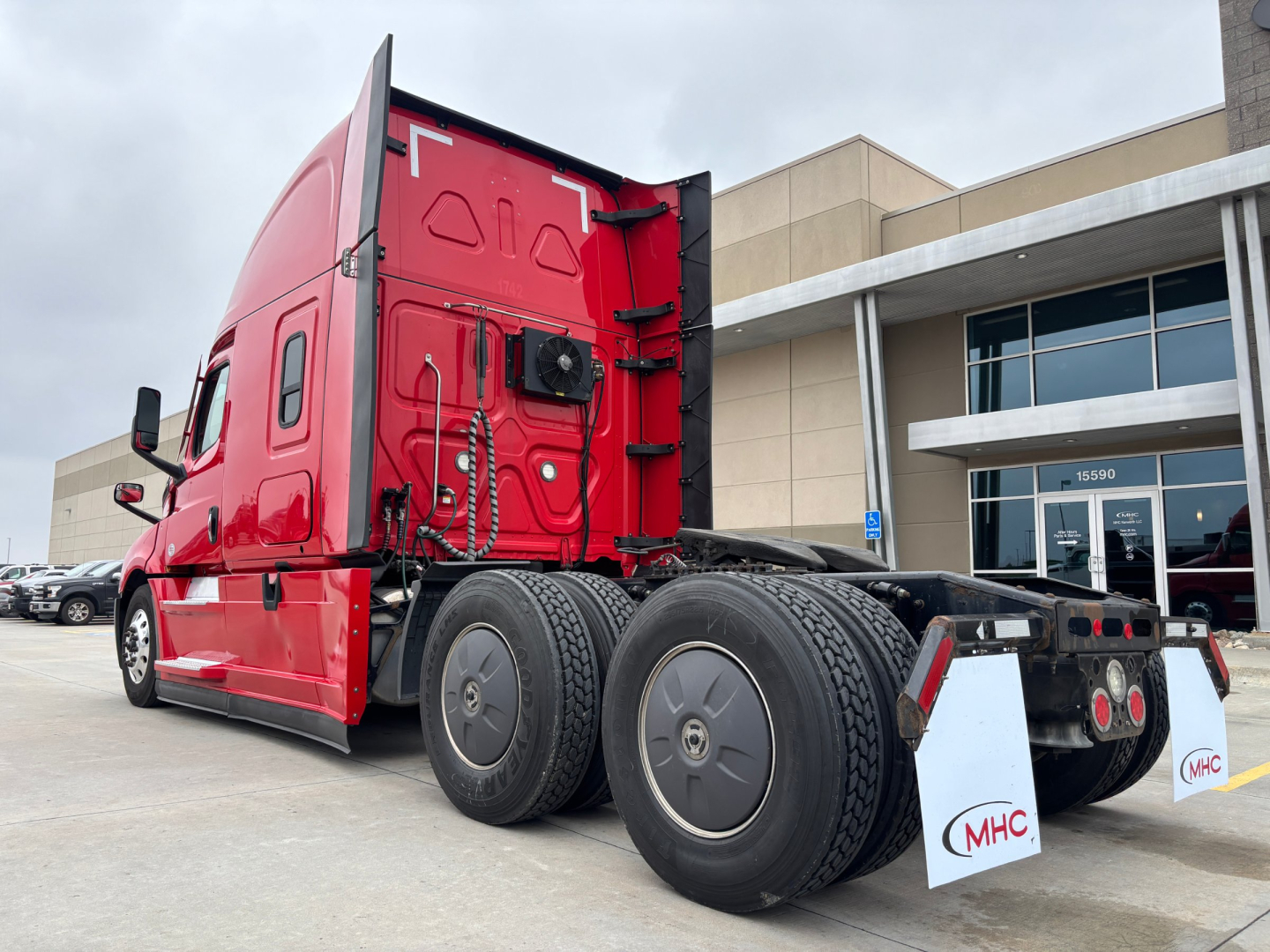 Truck tractor rear-left view showing dual rear axles and red sleeper cab with black chassis and mudflaps labeled MHC.