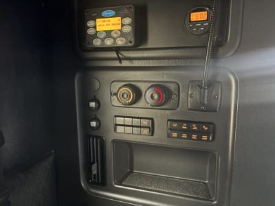 Truck cab interior panel with control dials and digital display. Close-up of dashboard controls, knobs, and a small orange timer display.