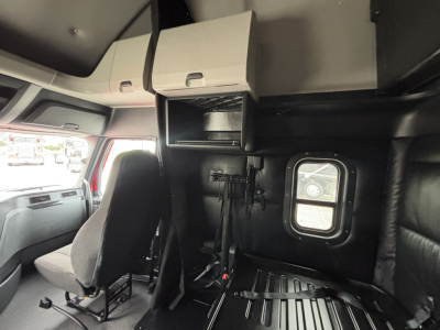 Interiors of a Freightliner PT126064ST sleeper cab showing black leather seats, overhead cabinets, and a small window with a sunshade.