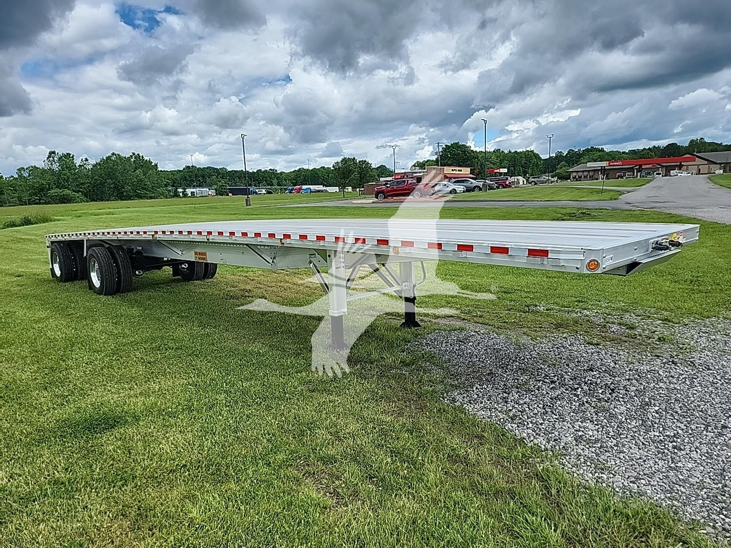 Flatbed trailer platform showing dual rear axles and long low deck with reflective tape along edges; brand watermark present.