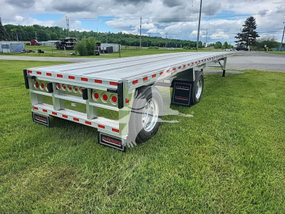 Flatbed trailer showing dual rear lights and aluminum deck with reflective tape along edges; rear bumper area with circular tail lights and black mud flaps; tandem axle configuration.