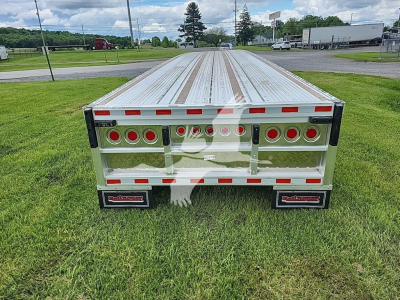 Flatbed trailer rear view showing aluminum deck and tail lights on both sides, with fenders and branding plate.