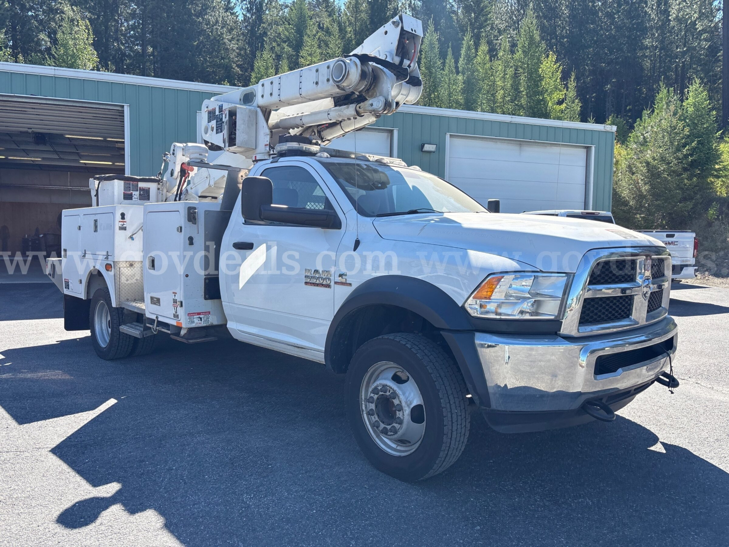 Ram 5500 bucket truck with utility body and mounted boom crane, white cab and chassis, front dual wheels, equipment compartments, side view