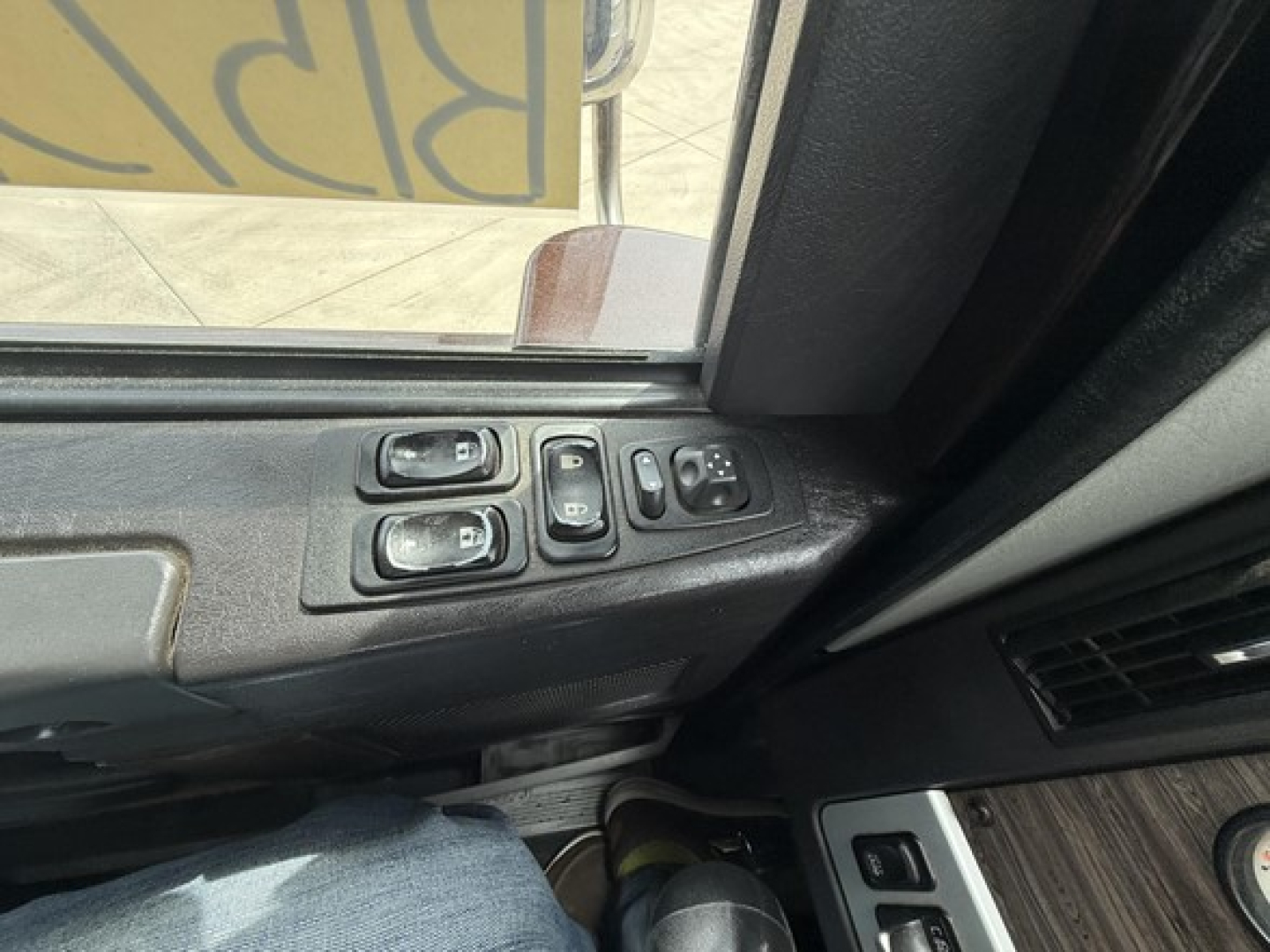 Cab interior door panel with window and mirror control switches in a Freightliner 122SD cab. Visible are three window/mirror control buttons and a wood-toned panel.