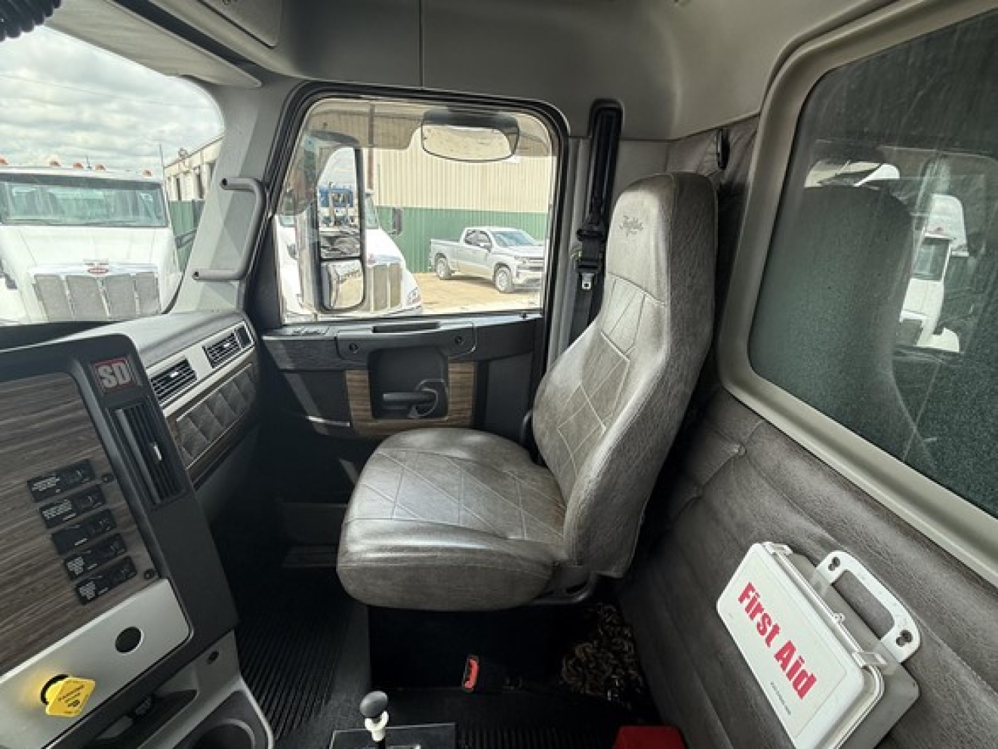 Cab interior of 2019 Freightliner 122SD dump truck showing gray cloth seat, dashboard with controls, driver door, and First Aid kit on side panel.