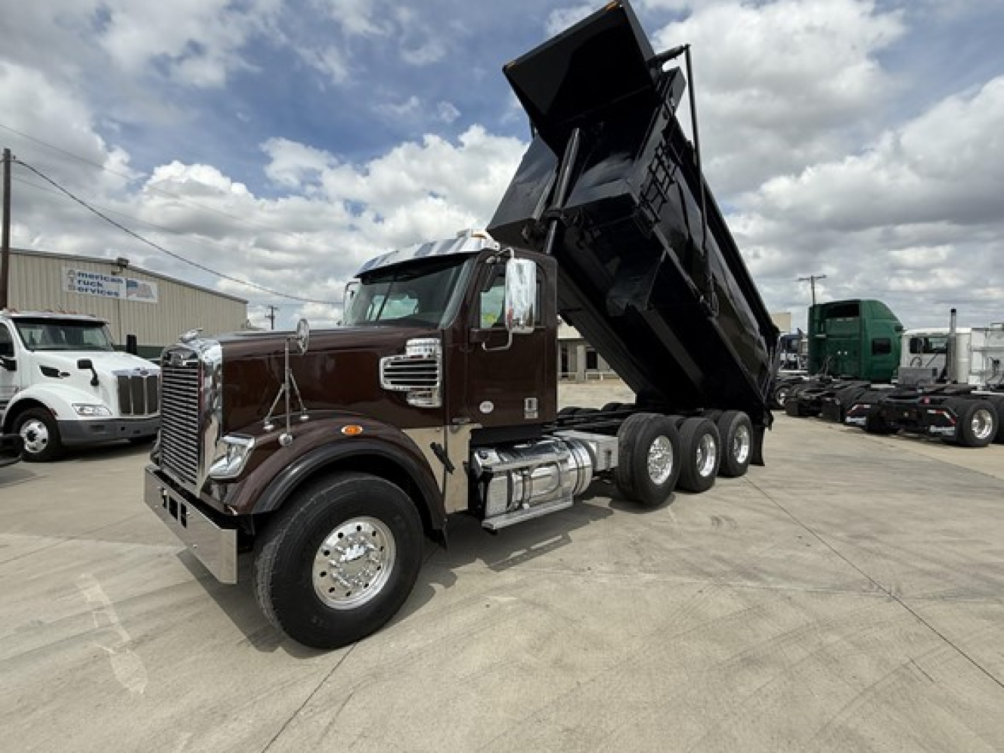 Freightliner 122SD dump truck with tilted bed in a dealership lot showing cab and dual rear axles.