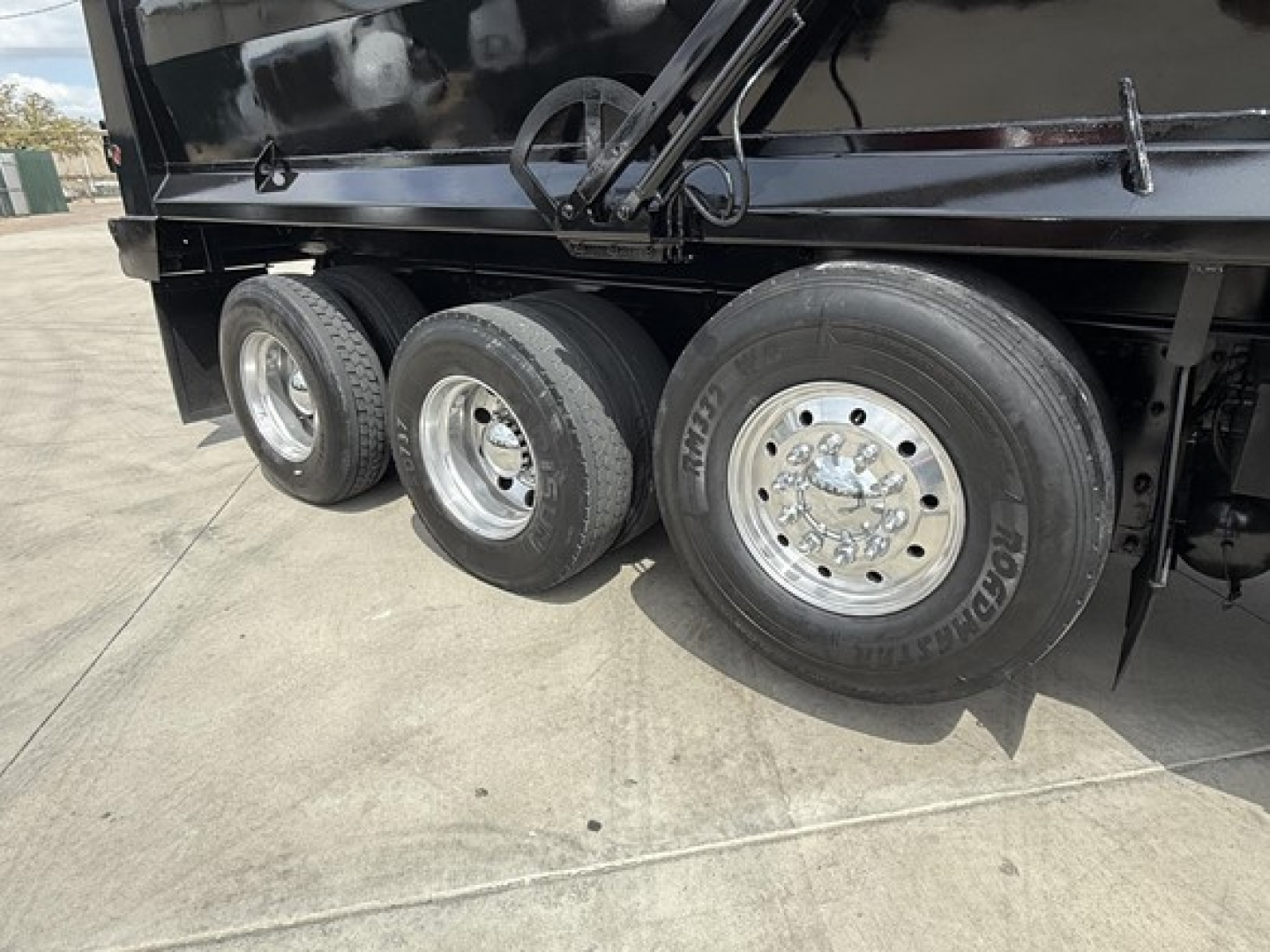 Wheel and tire arrangement on a Freightliner 122SD dump truck showing multiple silver rims and black undercarriage.