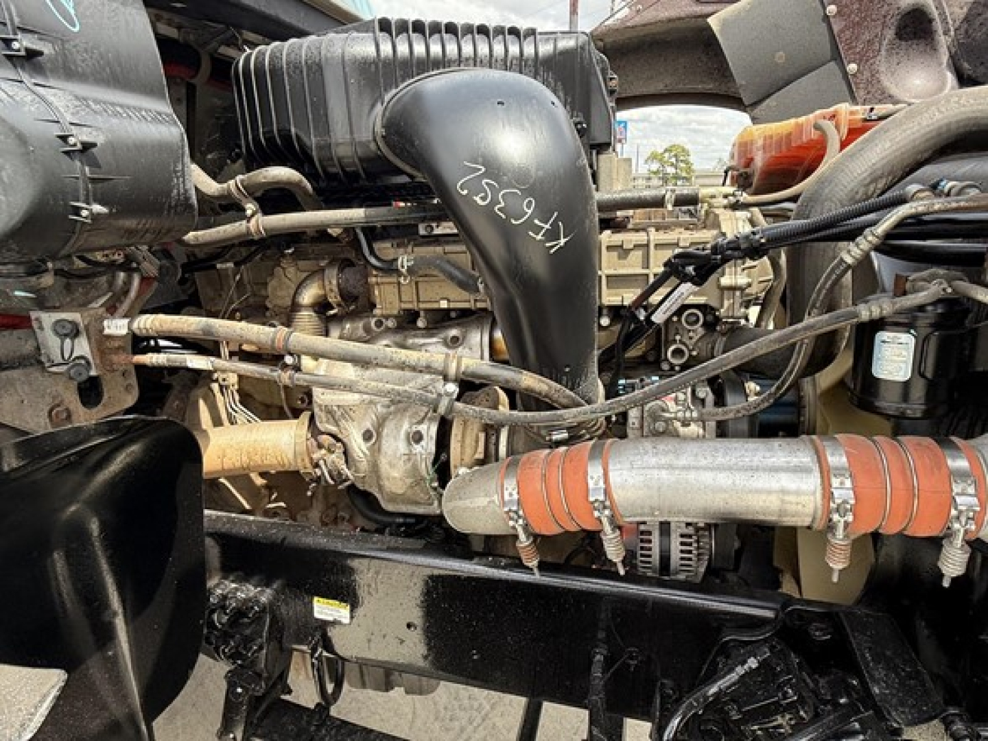 Engine bay of a Freightliner 122SD showing air intake hose, turbo, hoses, belts, and metal components with handwritten numbers on a black plastic air duct.