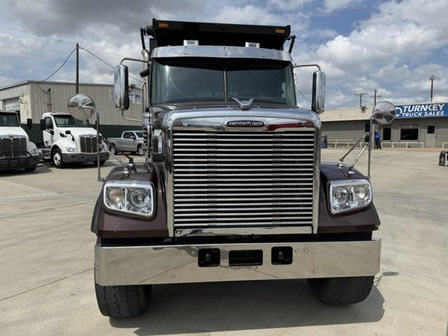 Front view of a 2019 Freightliner 122SD dump truck showing large chrome grille, rectangular headlights, heavy front bumper, and dump body hitch area.