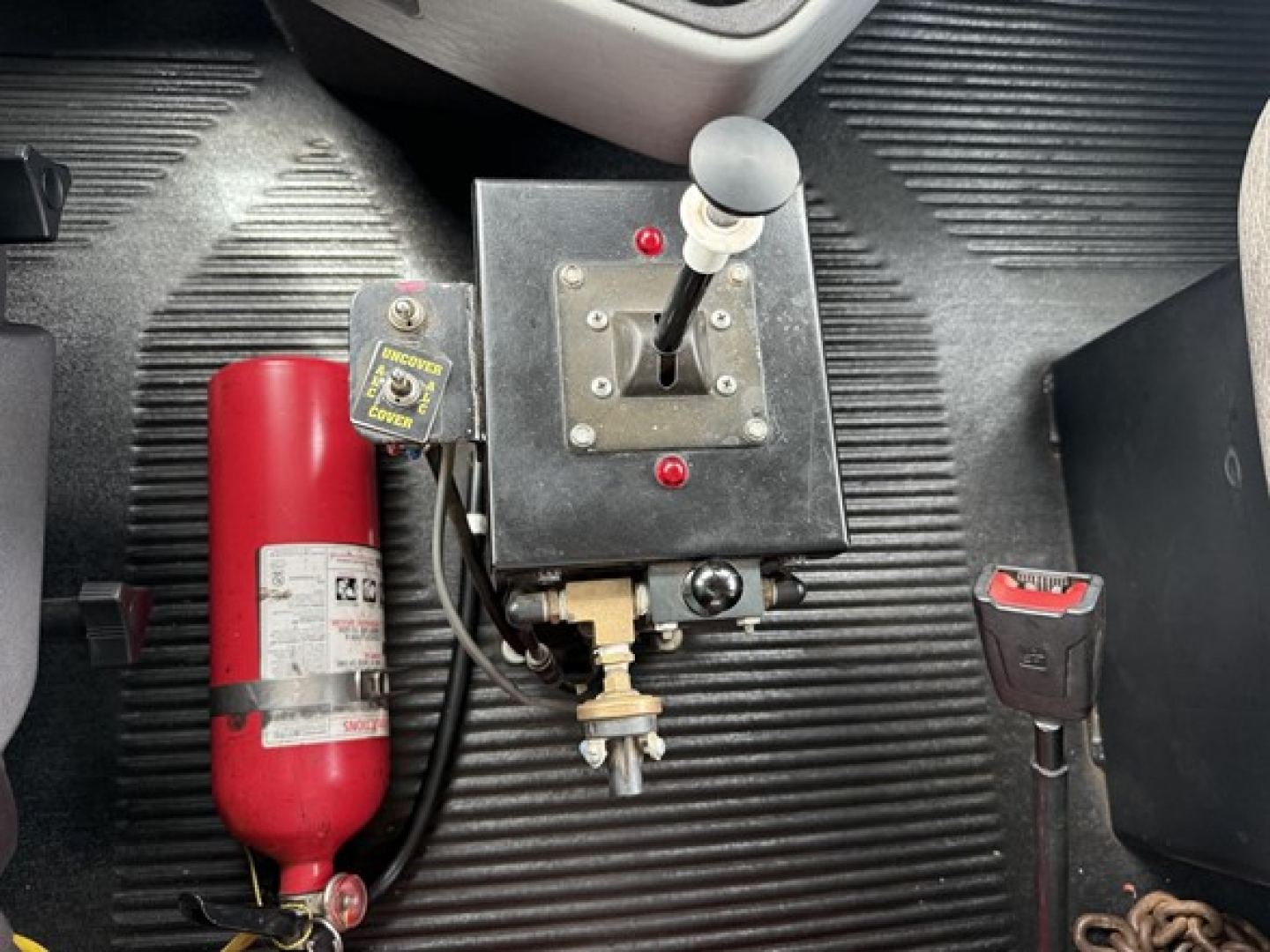 Freightliner 122SD manual gear shift console with red fire extinguisher mounted to left, black center console and parking brake handle visible, rubber truck floor mat.