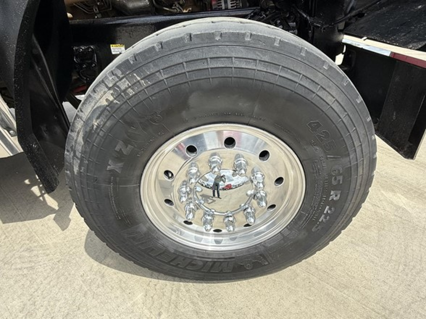 Wheel and tire assembly of a Freightliner dump truck showing large lug nut pattern and polished chrome hubcap.