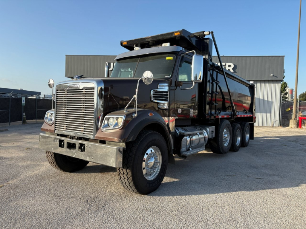 Freightliner 122SD dump truck in service showing front grille, dual rear axles, and dumping bed.