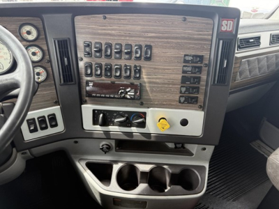 Dashboard panel of a 2019 Freightliner 122SD showing multiple toggle switches and gauges, woodgrain panel, center console with cup holders.