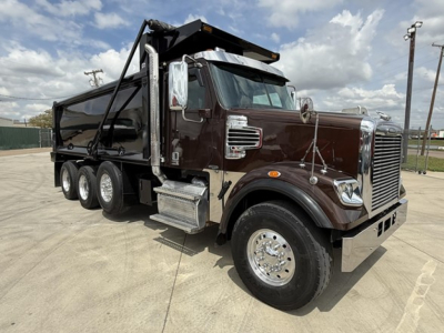 Dump truck with dark brown cab and black dump body showing Freightliner 122SD, chrome grille, side steps, and heavy-duty tires.