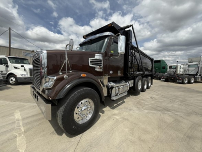 Freightliner 122SD dump truck in three-quarter view showing brown cab, large chrome grille, tilt hood, dual rear axles, and dumping bed.