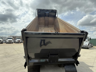 Dump truck bed of a 2019 Freightliner 122SD viewed from the rear with open tonneau and loading chute, showing metal bed walls and tailgate latch.