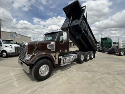 Freightliner 122SD dump truck with tilted bed in a dealership lot showing cab and dual rear axles.