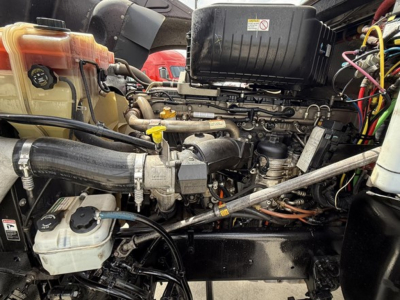 Truck engine bay of a 2019 Freightliner 122SD with visible coolant reservoir, hoses, and diesel engine components as seen from side view.