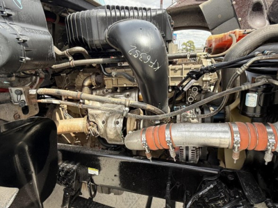 Engine bay of a Freightliner 122SD showing air intake hose, turbo, hoses, belts, and metal components with handwritten numbers on a black plastic air duct.