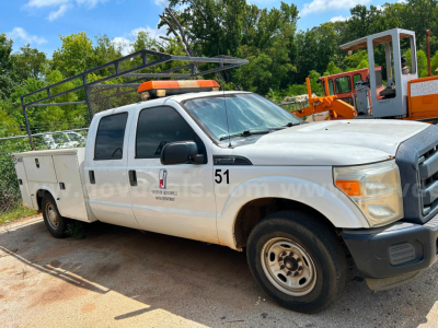Ford F-250 service/utility truck with orange light bar, utility bed, and ladder rack in a lot.