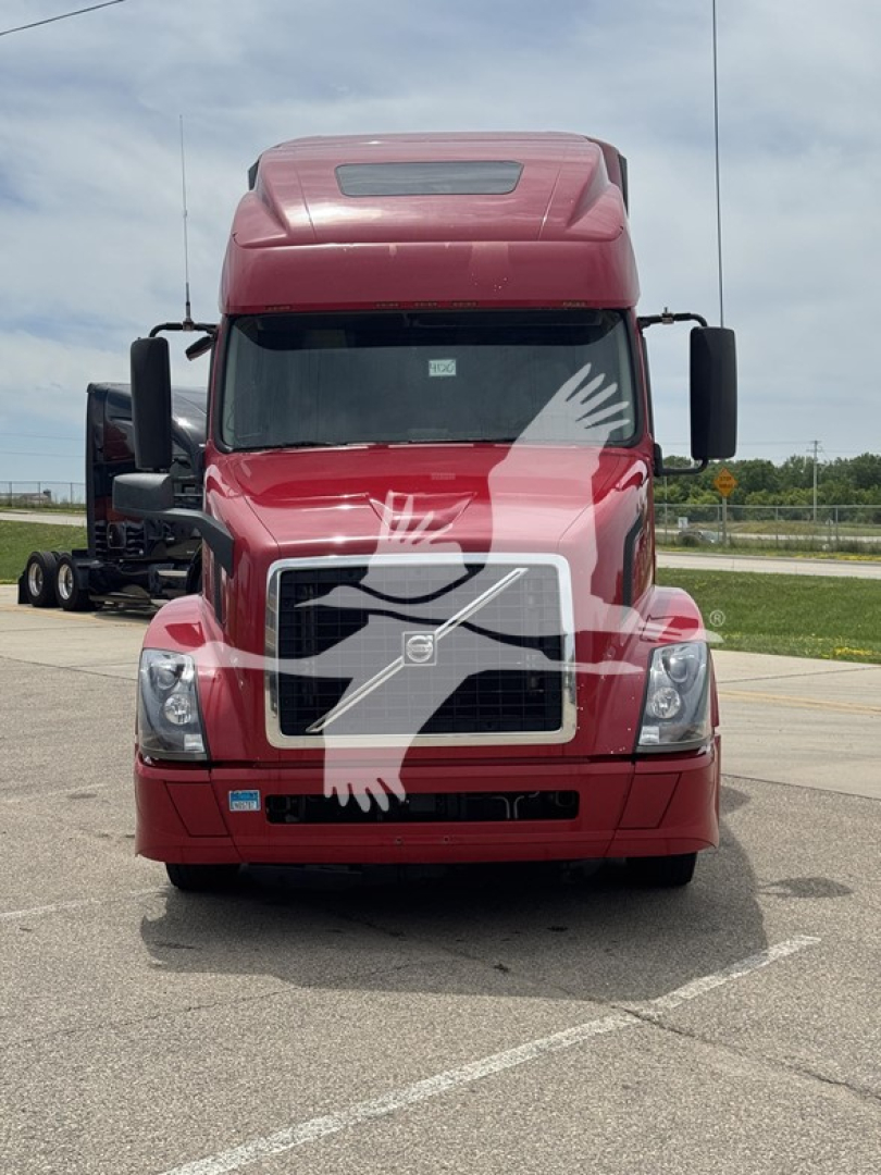 Front view of red Volvo VNL64T670 truck with windshield protection overlay, showing grille, headlights, and large mirrors.