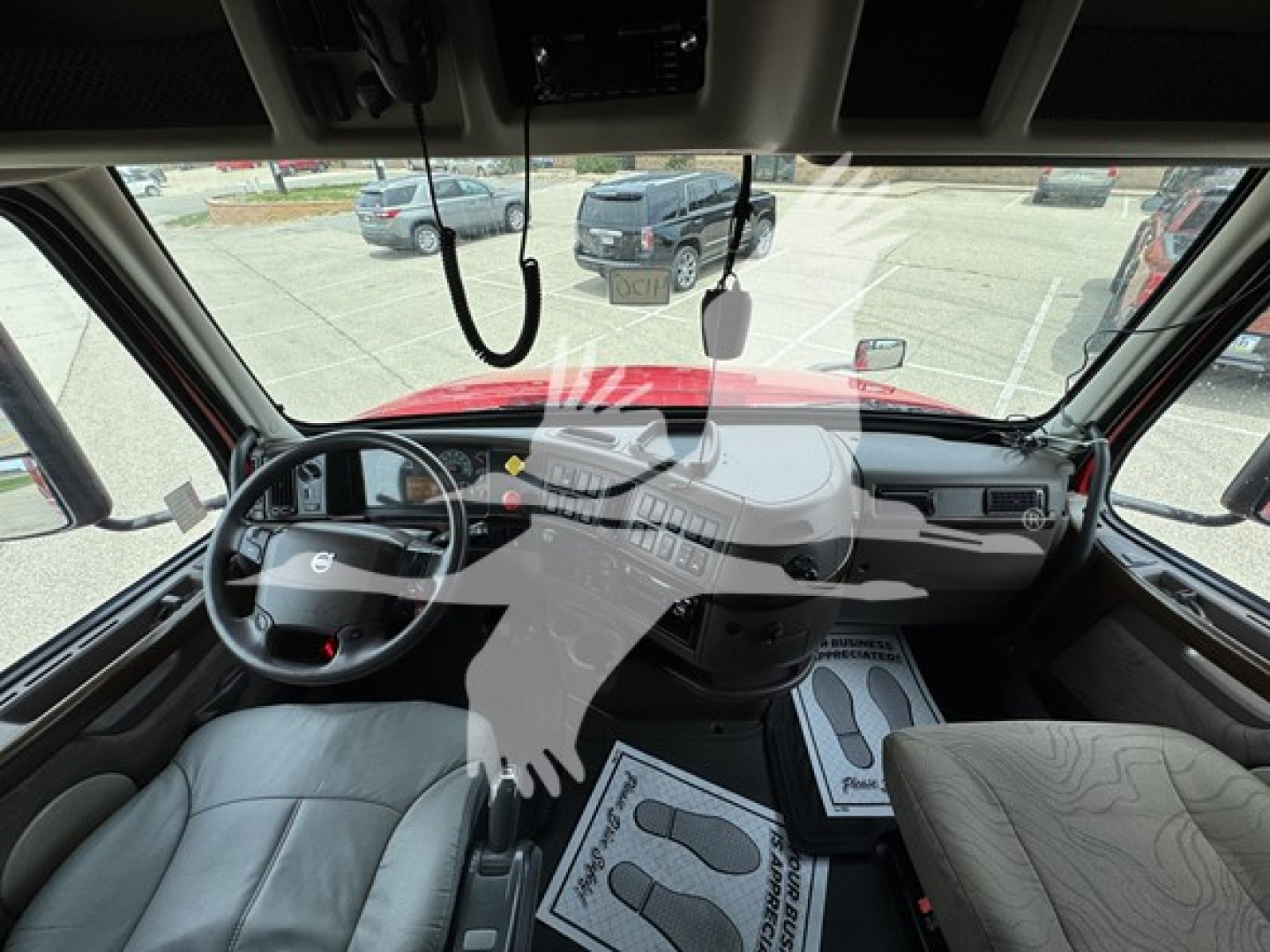 Cab interior of a Volvo truck showing steering wheel, dashboard, and driver and passenger seats. Windshield view includes large dash area with controls and mirrors.