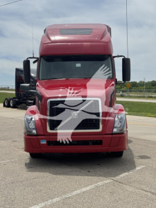 Front view of red Volvo VNL64T670 truck with windshield protection overlay, showing grille, headlights, and large mirrors.