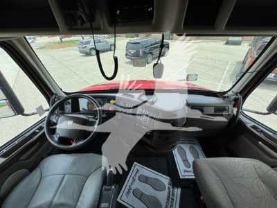 Cab interior of a Volvo truck showing steering wheel, dashboard, and driver and passenger seats. Windshield view includes large dash area with controls and mirrors.