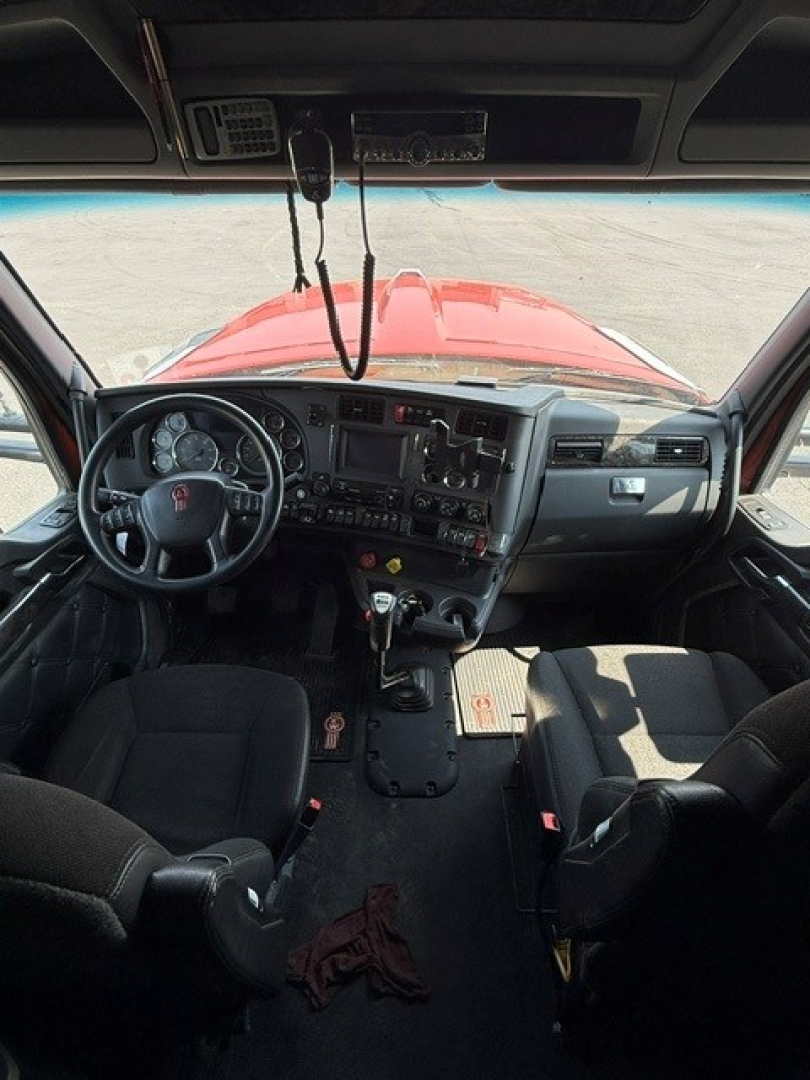 Kenworth W990 cab interior view from driver's seat showing dashboard with gauges, steering wheel, center console, gear shifter, and two seats.