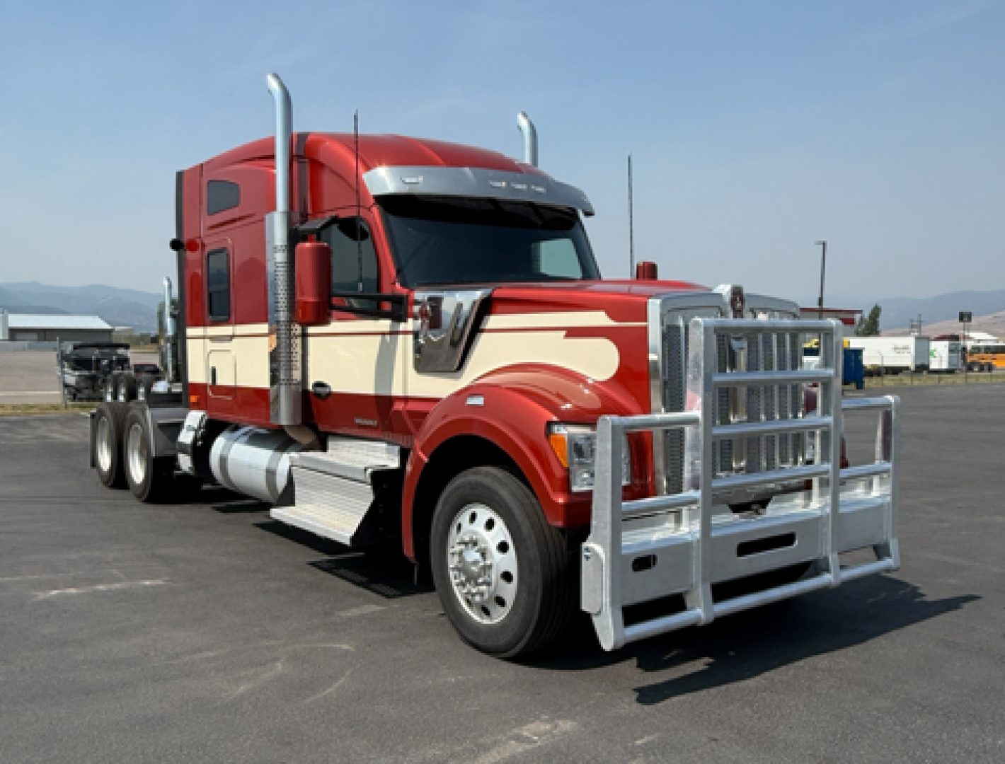 Kenworth W990 tractor unit in red and cream colors with large chrome grille guard, side exhaust stacks, and dual rear axles.