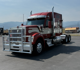 Kenworth W990 truck shown in front-left view with chrome grille guard, red cab, and sleeper; Dual rear wheels and chrome fuel tanks visible.