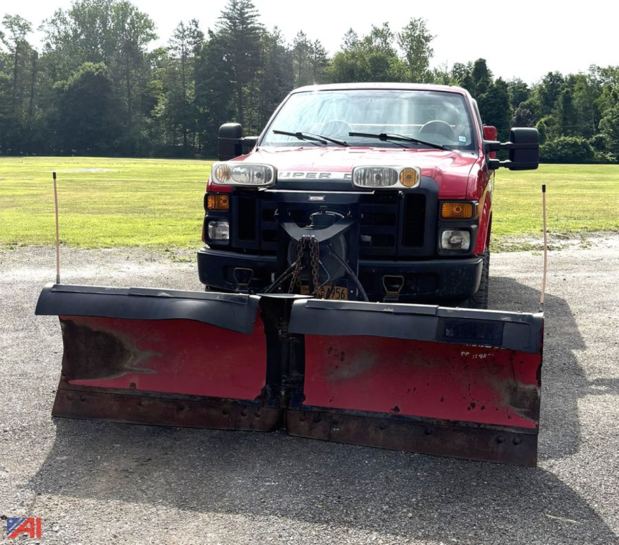 Ford F-250 Super Duty utility truck with front snow plow attachment, red cab, black bumper, in an open lot with trees in background.