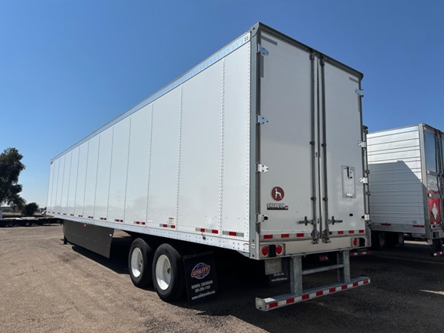 Trailer showing a long aluminum box trailer with dual rear doors, side profile, and dual rear axles in a parking lot.