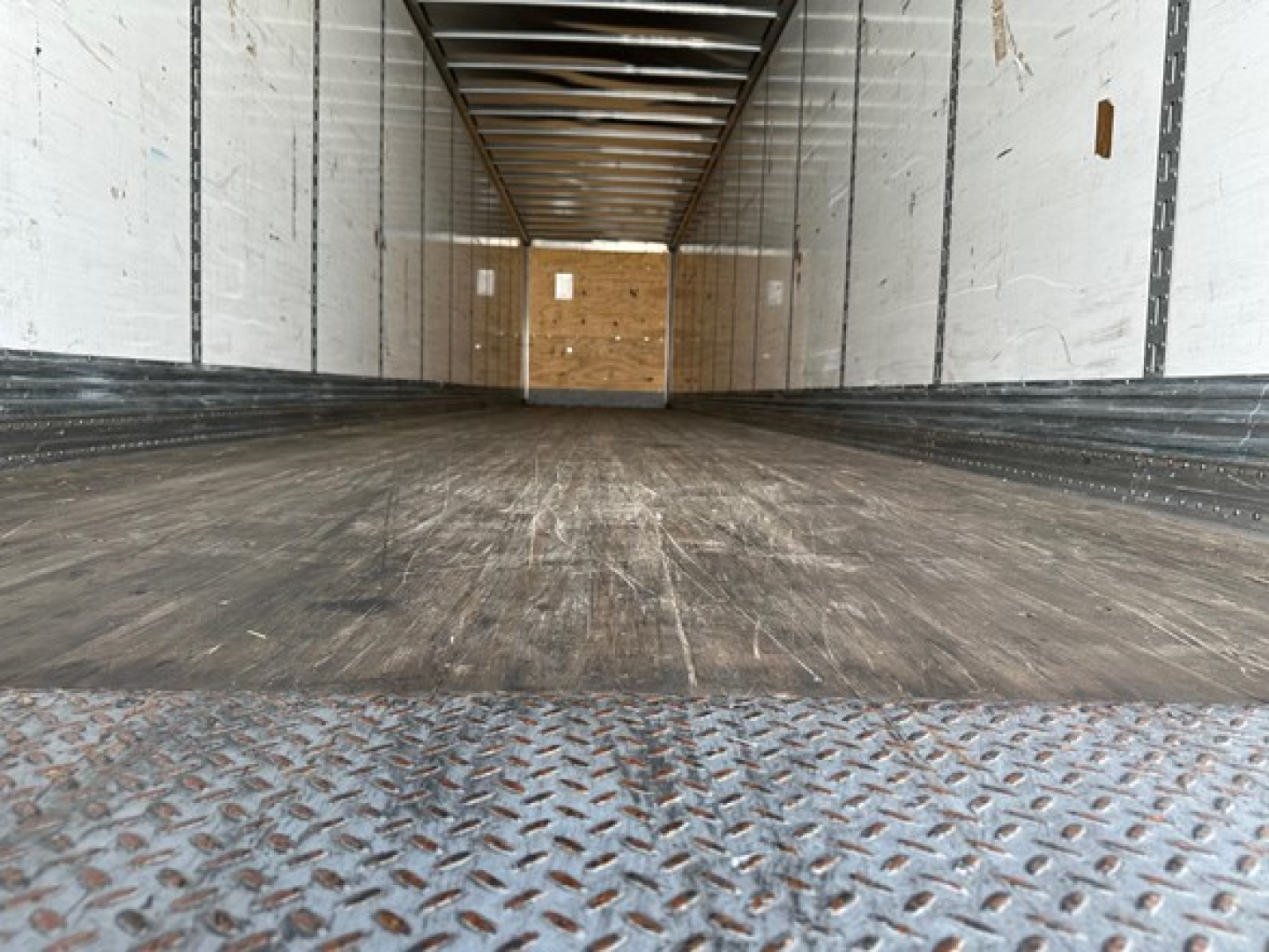 Trailer interior showing empty cargo deck with wooden bulkhead at far end and diamond plate threshold.