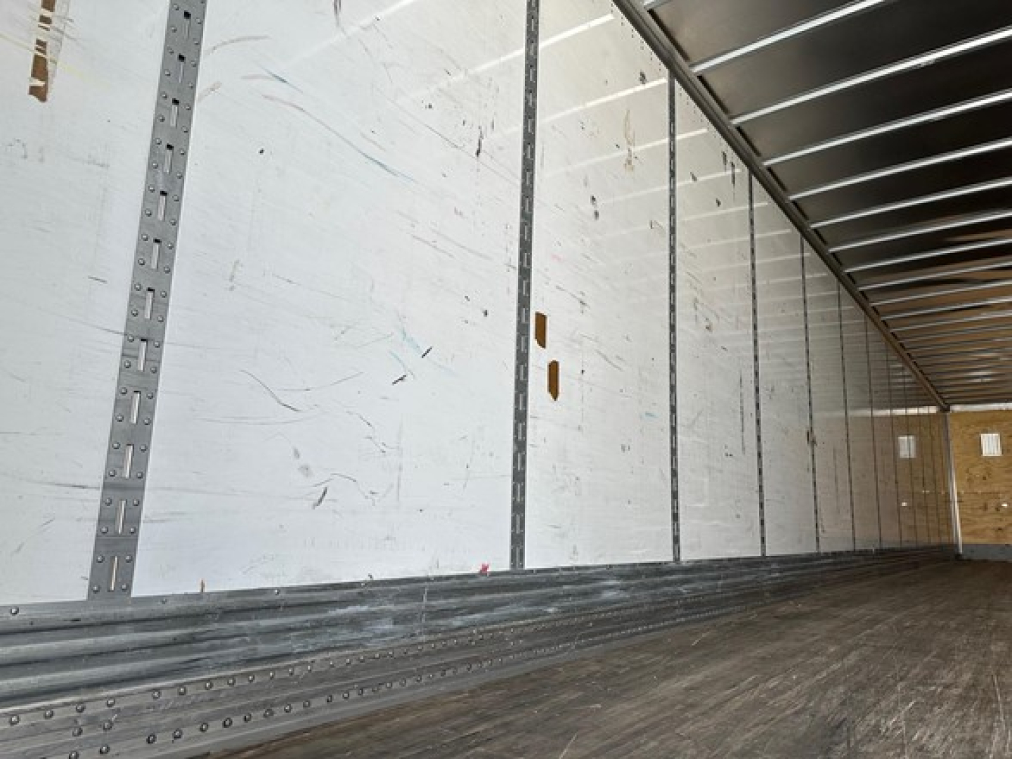 Interior trailer image showing metal side panels with vertical aluminum rails and wooden floor; empty van trailer with bright interior.