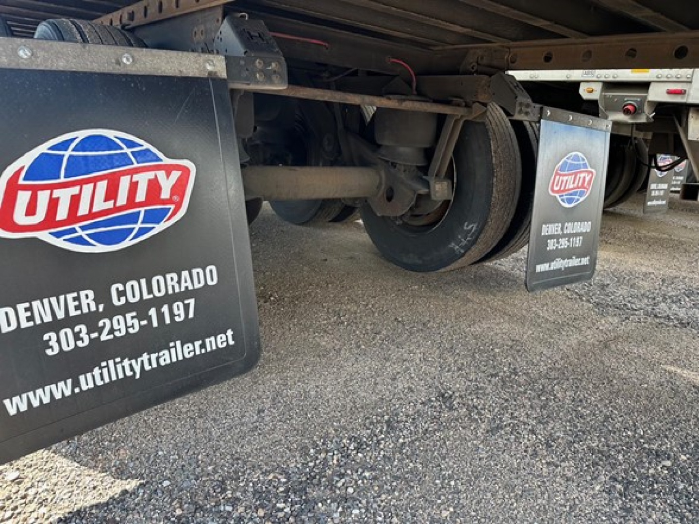 Trailer undercarriage showing axle, wheels, and mudflaps with Utility trailer branding and Denver Colorado contact info.